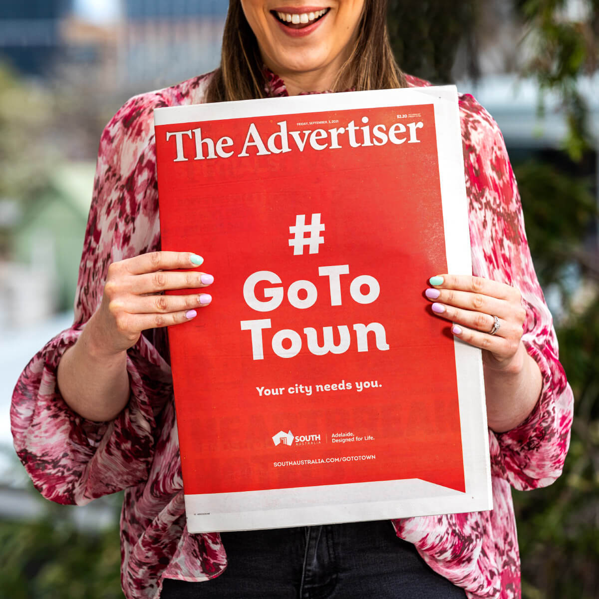 Smiling woman holding a copy of The Advertiser with Go To Town advertisement on the front page