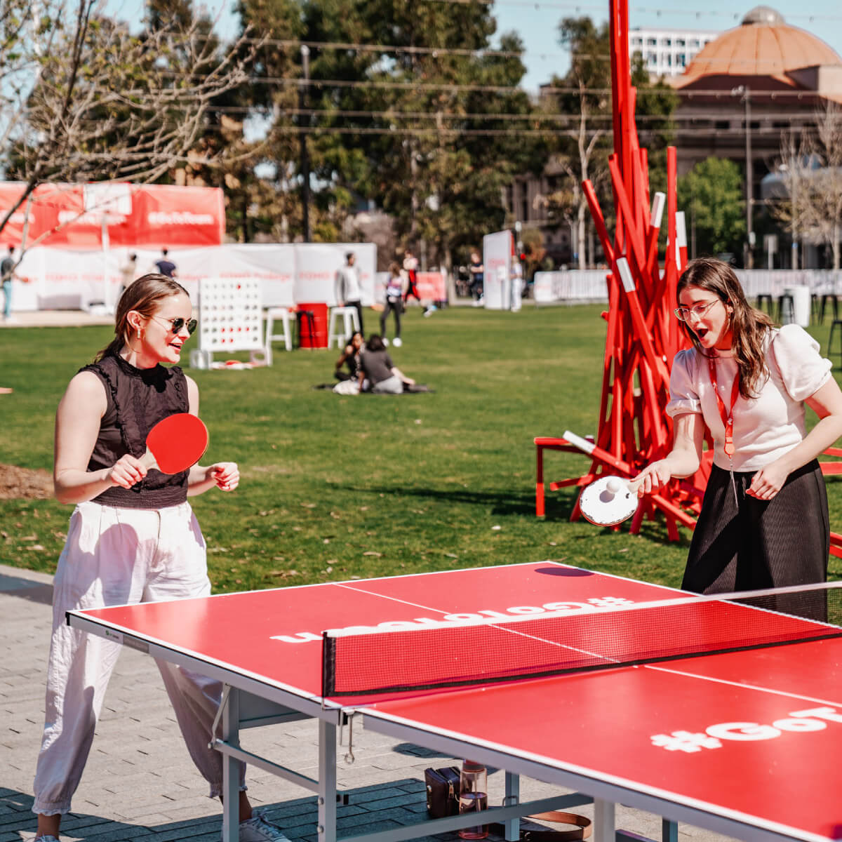 Two woman playing table tennis on a red table with Go To Town branding