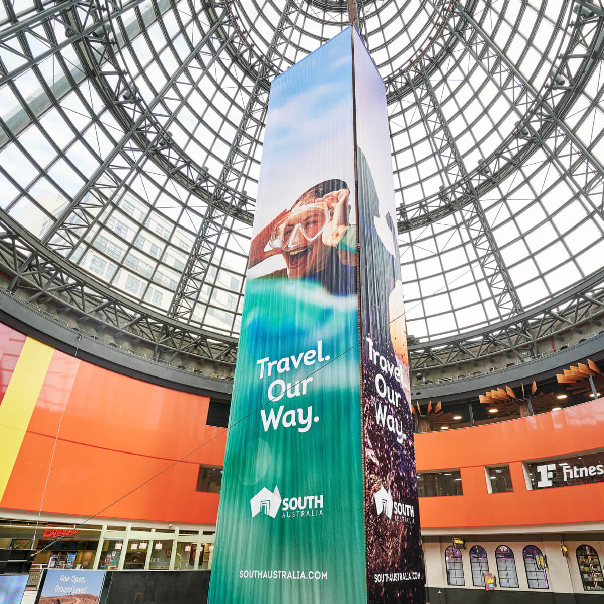 A large indoor pillar displaying the 'Travel Our Way' tagline against a photo of a woman snorkelling.