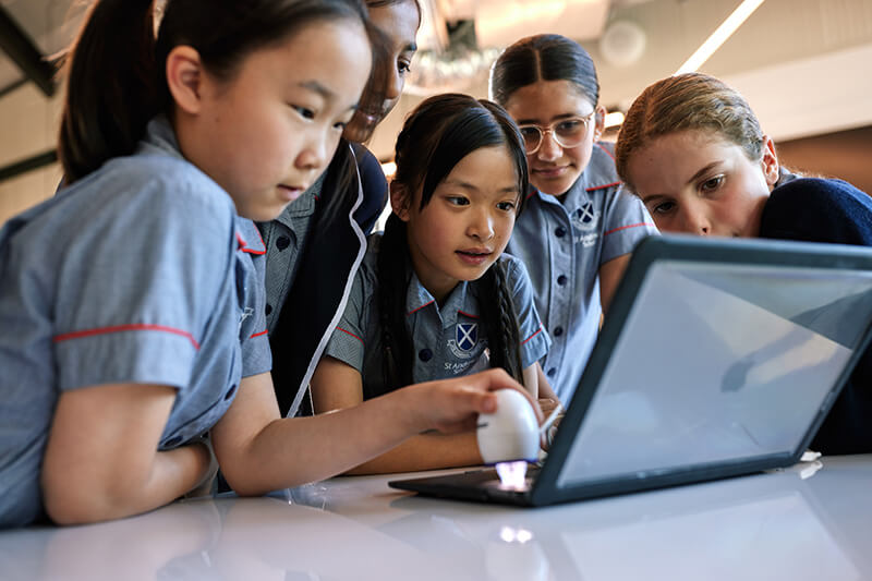 A group of primary school girls clustered around a laptop