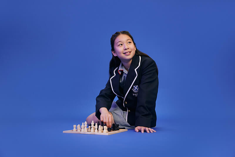 A primary school student kneeling by a chess board against a bright blue background