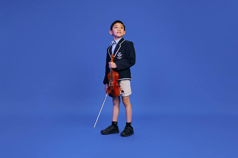 A boy standing holding a violin against a bright blue background