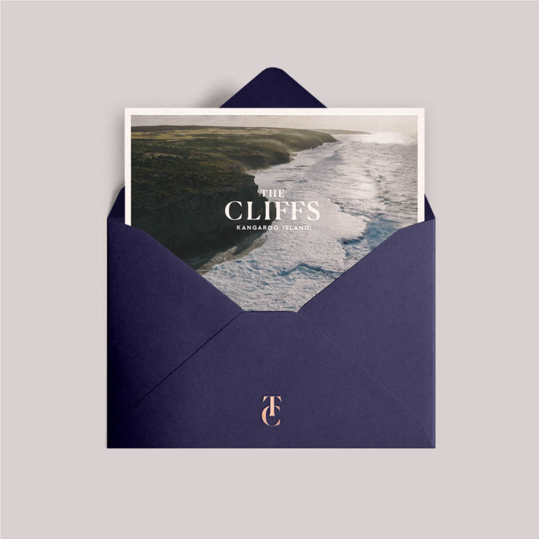 A card with The Cliffs logo on a coastal background in a dark blue branded envelope