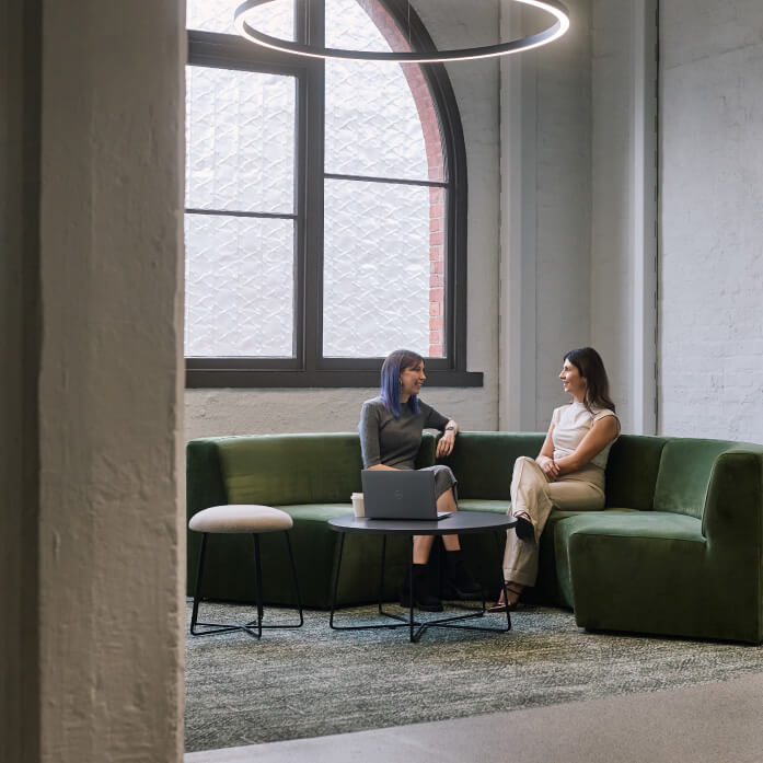 Two professional looking women photographed talking in a hub space