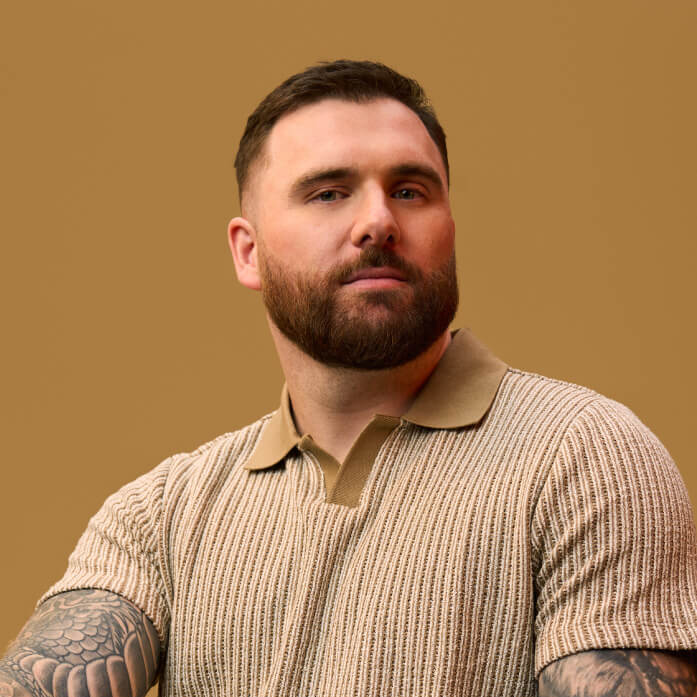 A bearded man photographed in studio with a coloured background