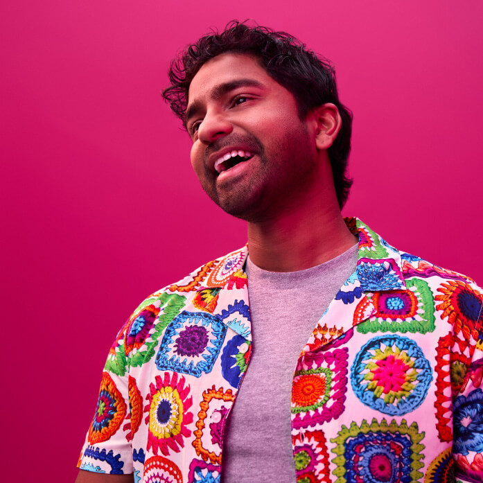 A colourfully dressed young man photographed in studio with a coloured background